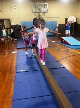 Girl balances on low balance beam in gym.