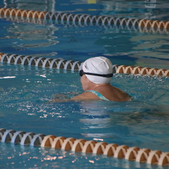 Woman swimming backstroke in an indoor pool.