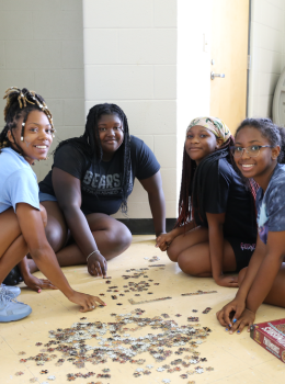 Four smiling girls assemble a puzzle on the floor.