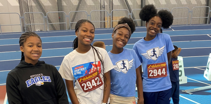Four girls smiling on an indoor track.