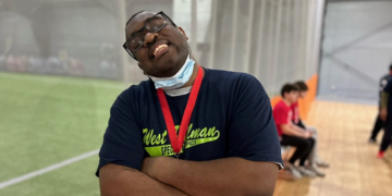 Smiling athlete wearing a medal and face mask, arms crossed.