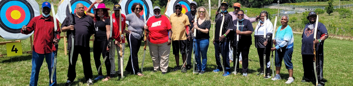 A group of archers stand on a grassy field with their bows, posing for a photograph in front of archery targets.