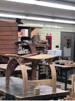 Wooden chair with curved slatted seat and matching footstool in a workshop.